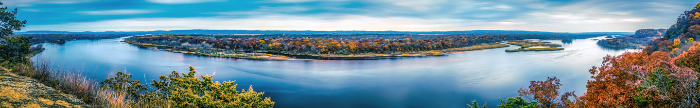 A panoramic view of a wide river flowing through a wooded Wisconsin landscape with trees in full fall color